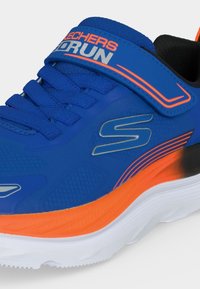 Chaussure de running Skechers bleue avec semelle orange et blanche, lacets bleus et une bride velcro étiquetée "SKECHERS GO RUN."
