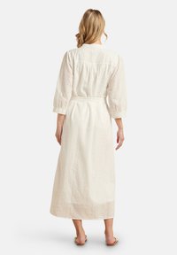Abito lungo bianco con un design testurizzato, maniche a tre quarti e una cintura in vita. I dettagli del tessuto presentano fantasie a occhio di pernice.