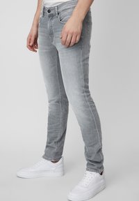 Jeans in denim grigio con un fit slim, caratterizzati da un classico design a cinque tasche e delicate sfumature. Abbinati a sneakers bianche.