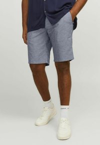 Shorts bleu clair en tissu texturé, dotés de poches lat�érales et d'une coupe décontractée, associés à des baskets blanches et des chaussettes côtelées.