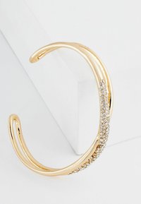 Gul metal cuff armbånd med et tekstureret design og en række klare rhinsten langs den ene side. Glat finish og åbne ender.