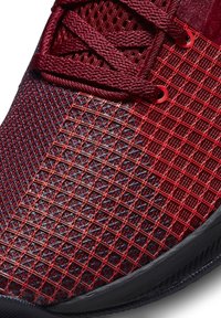 Gros plan d'une basket en mesh rouge avec une superposition en grille, des lacets rouges assortis et une semelle en caoutchouc noire.
