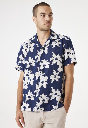 Camisa de manga corta en azul marino con grandes patrones florales blancos, hecha de una tela ligera, con cuello y frente abotonado.