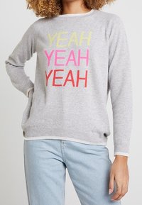 Grauer Pullover mit der Aufschrift "YEAH YEAH YEAH" in lebendigem Gelb, Pink und Rot. Weiches Material, lange Ärmel und gerippter Saum sowie Bündchen.