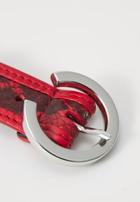Sangle en cuir rouge avec une boucle circulaire en argent brillant, présentant un motif texturé et des bords surpiqués pour plus de détails.