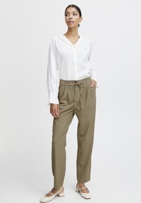 Biela blúzka s výstrihom do V a zapínaním na gombíky, s volánovými rukávmi. Khaki nohavice s vysokým pásom, viazaním a záhybmi. Béžové topánky na blokovom opätku.