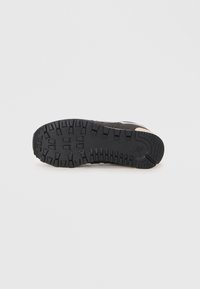 Semelle de chaussure en caoutchouc noir avec des profondeurs pour une meilleure traction ; bords lisses ; présente un accent brun clair sur le talon.