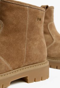 Bruine suède enkellaarzen met een ronde neus, rubberen zool en decoratieve steken; voorzien van een klein logo in goud aan de zijkant.