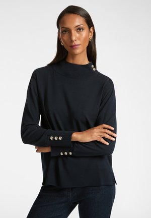 Maglione a coste blu navy con collo alto, dettagli con bottoni dorati su spalle e polsini, maniche lunghe e spacchi laterali all'orlo.