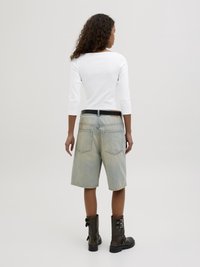 Denim-Shorts in heller Waschung mit lockerer Passform, mit Gesäßtaschen. Kombiniert mit einem enganliegenden weißen Langarmshirt und schwarzen Schnallenstiefeln.