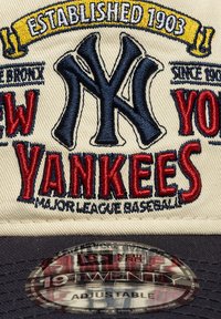 Καπέλο μπέιζμπολ με μπροστινό μέρος σε εκρού χρώμα που φέρει κεντημένο το λογότυπο "New York Yankees" σε κόκκινο και μπλε, με ρυθμιζόμενο μπλε σκιάδιο και πλαστική ετικέτα.