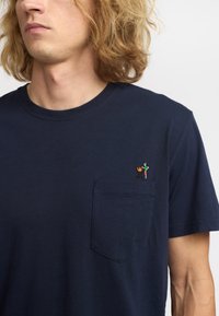 Camiseta de algodón azul marino con cuello redondo, que presenta un bolsillo en el pecho y un dise�ño bordado colorido de una parrilla y figuras.
