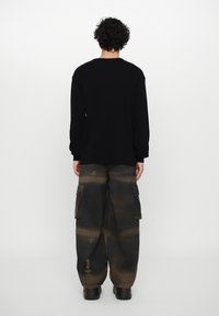 Sort ribbet sweater med lange ærmer, parret med oversized cargo bukser i en blanding af mørkebrun og sorte nuancer samt sidelommer.