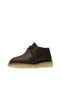 Brown leather desert boots with a round toe, contrasting white stitching, and a light-colored rubber sole. Unique design with minimal hardware.