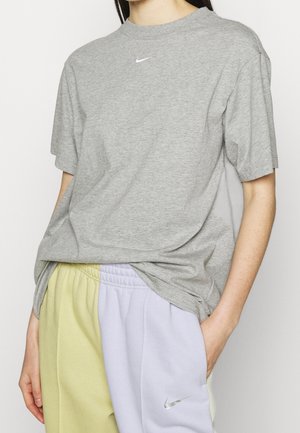 Person wearing a grey Nike t-shirt and two-tone yellow and lavender Nike sweatpants with hands relaxed by sides.