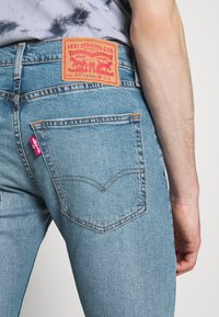 Vaaleansiniset farkut, joissa on punainen nahkapaikka, jossa lukee "Levi Strauss & Co.", takataskussa on ommelta ja pieni punainen etiketti.