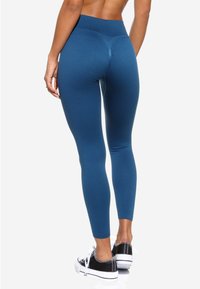 Leggings teal taille haute fabriqués dans un matériau extensible ; texture lisse avec un design ajusté et sans motifs visibles.