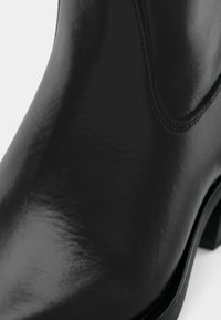 Melna ādas potīšu zābaciņš ar spīdīgu apdari, izliekta forma un dekoratīvā dūriena apdare gar šuvēm. Stabils blokveida papēdis.