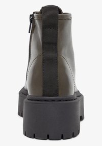 Bottines en cuir vert olive avec une épaisse semelle noire, des panneaux latéraux élastiques et une fermeture éclair pour un enfilage facile. Fini texturé pour améliorer l'adhérence.