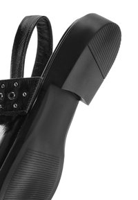 Chaussure à talon haut noire à finition brillante, avec une semelle texturée, un large talon et des clous décoratifs sur la bride.