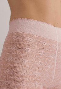 Rosa spetsshorts med blommiga och geometriska mönster, med en vågig midja och en delikat, texturerad yta.