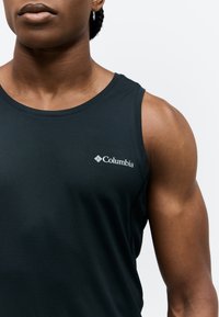 Gros plan d'une personne portant un débardeur sportif noir Columbia, montrant le haut du torse et les muscles du bras gauche.