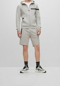 Ljusgrått träningsset bestående av en dragkedjetröja med logotyp, matchande shorts, sneakers med svarta detaljer och strumpor med logotyp.