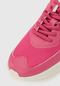 Pink athletic shoe with textured fabric and smooth synthetic accents. Features intricate stitching and traditional lace-up design.