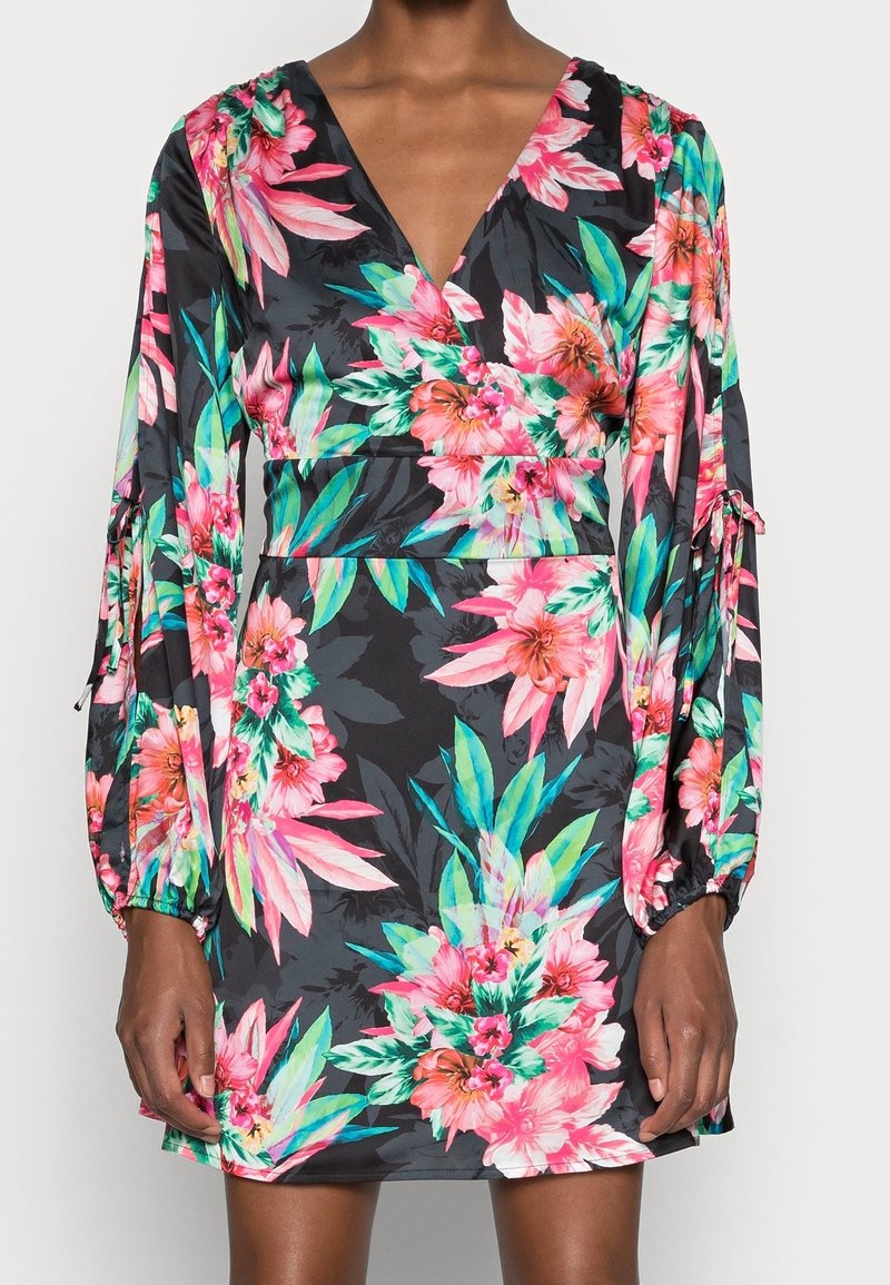Robe noire avec imprimé floral rose vif et vert, manches longues bouffantes avec liens, taille ajustée et décolleté en V portée par une personne debout.