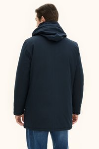 Merivihreä, vedenpitävä takki hupulla, jossa on suora leikkaus, sivutaskut ja pehmeä tekstuuri.