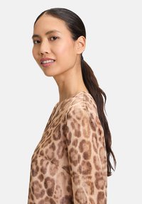 Blusa con stampa leopardata in marrone chiaro con accenti dorati. Presenta un collo a V e maniche lunghe, realizzata in un tessuto leggero e testurizzato.