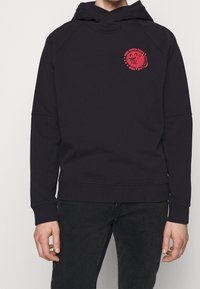 Sudadera negra hecha de un tejido suave, con un logotipo gráfico rojo en el lado izquierdo del pecho, puños acanalados y un ajuste relajado.