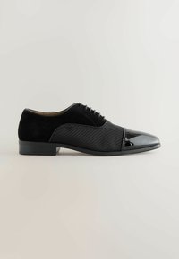 Schwarze formelle Oxford-Schuhe für Herren mit gewobener Textur im Mittelteil, Wildleder-Ferse und glänzender Kappe, seitlich auf einem neutralen Hintergrund gezeigt.