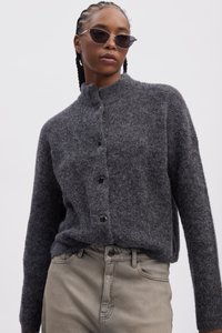 Gray wool cardigan with a high collar and six black buttons, worn over light-colored pants. The fabric appears soft and textured.