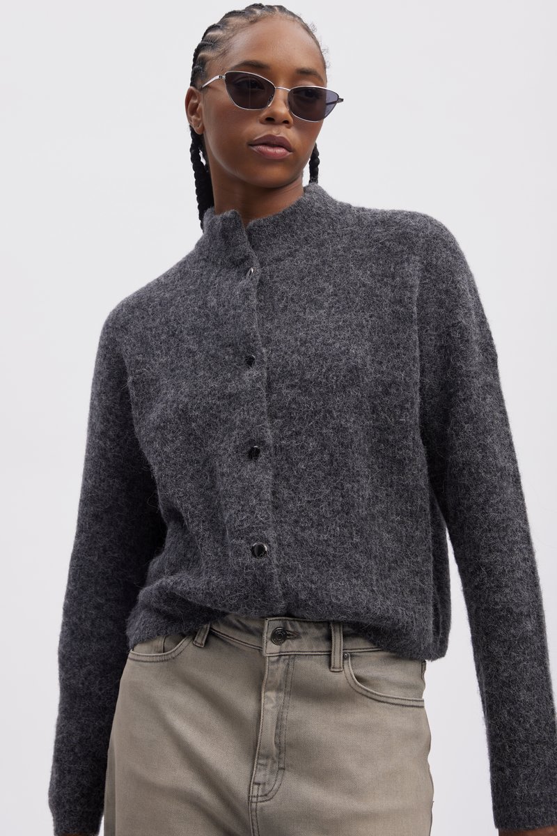 Gray wool cardigan with a high collar and six black buttons, worn over light-colored pants. The fabric appears soft and textured.
