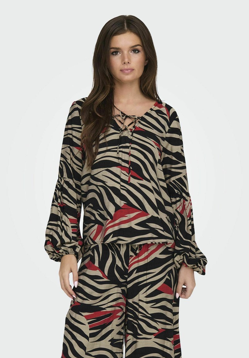 Maglietta a maniche lunghe color beige con strisce zebrate nere e rosse, caratterizzata da una scollatura a V con dettaglio a fiocco e maniche arricciate. Abbinata a pantaloni coordinati.