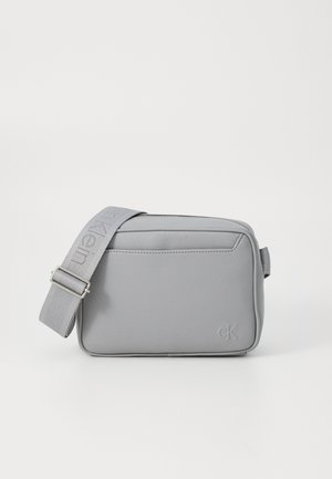 Borsa a tracolla in pelle sintetica grigia con design piatto, tracolla in tessuto regolabile e logo in rilievo sul davanti. Chiusura con zip.
