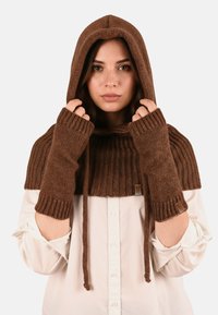 Poncho tricotat maro cu glugă și mănuși fără degete; prezintă o textură ribbed, șnur de ajustare și etichetă cu brand pe mânecă.