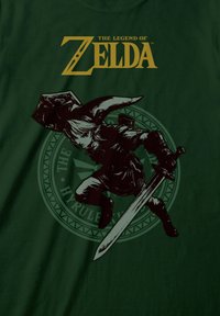 Zielona koszulka z czarną sylwetką postaci dzierżącej miecz, z napisem "The Legend of Zelda" w żółtym kolorze na górze.
