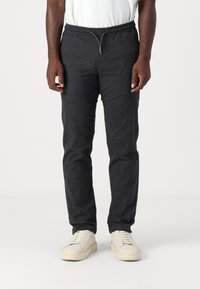 Sötét szürke, rugalmas anyagú jogger nadrág, elasztikus derékpánttal és zsinórral, slim fit szabású és puha tapintású. Fehér sportcipőkkel párosítva.