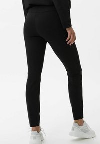 Black leggings with a slim fit, smooth texture, and high waistband. Worn with light gray athletic shoes. Minimalist design, no visible patterns.