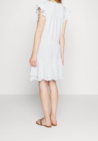 White short dress with ruffled sleeves, elastic waistband, and layered skirt featuring a scalloped hem. The fabric is lightweight and breathable.