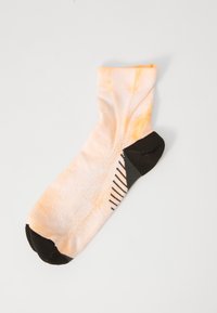 Sokker med et tie-dye mønster i lys orange og svart, med solid svart tå og hæl, samt teksturert grepdetalj på sålen.