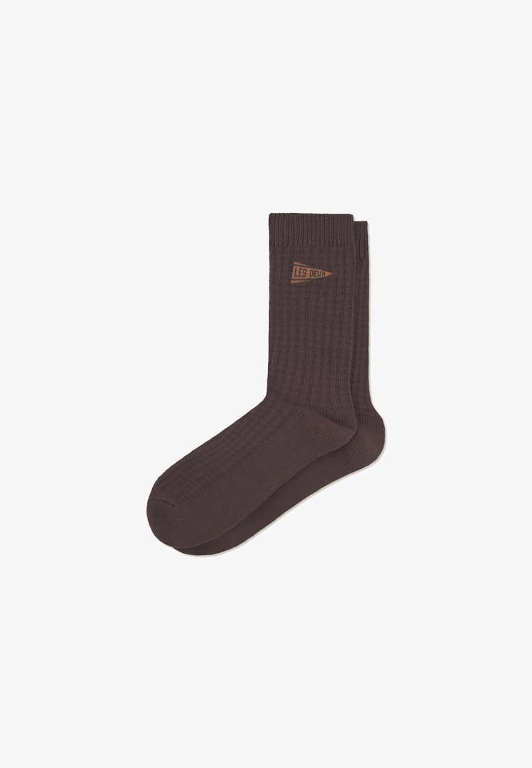 Meias castanhas com texturas em um estilo canelado, apresentando um pequeno rótulo castanho com o texto "LES DEUX". Feitas de um material macio e texturizado. Design de altura no tornozelo.