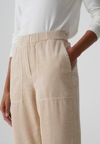 Beige corduroy broek met een gestructureerd ribbelontwerp, voorzien van zijzakken en een elastische tailleband, gedragen met een lichte trui.
