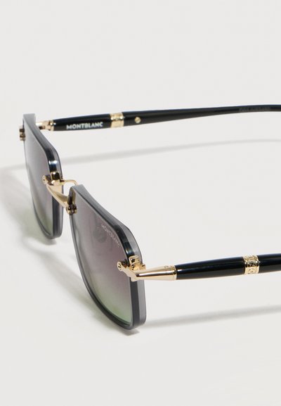 Μαύρα και χρυσά τετράγωνα γυαλιά ηλίου Montblanc με σκουρόχρωμους φακούς με διαβαθμίσεις, τοποθετημένα σε λευκή επιφάνεια.