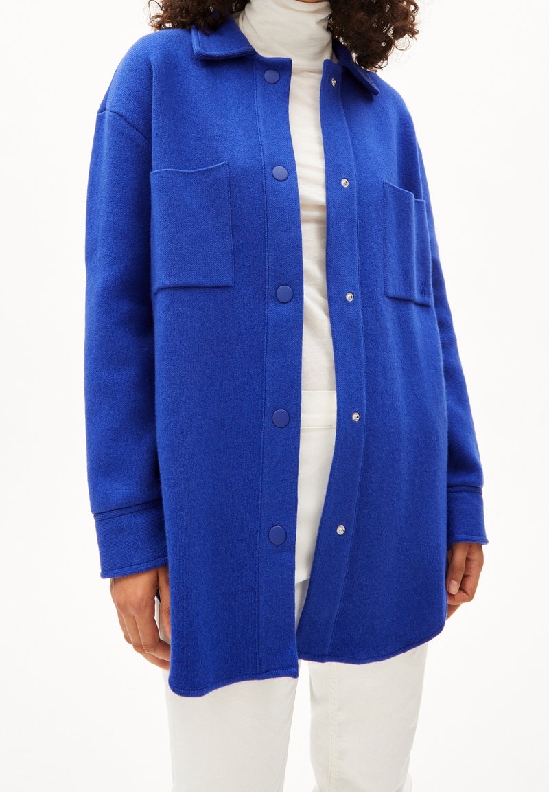 Blå ullblandning översized skjortjacka med två framfickor, knapplås och spetsig krage. Vit polo tröja under.
