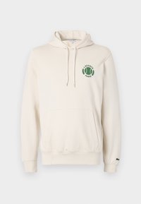 Krémová mikina s kapucí vyrobená z měkké tkaniny, obsahující klokaní kapsu a zeleně vyšívané logo s textem "LACOSTE" a "PARIS".