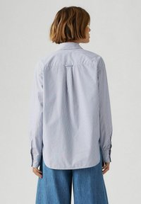 Camicia a maniche lunghe a righe, di colore azzurro e bianco, con orlo arrotondato. Il retro presenta una piega centrale e bottoni ai polsini.