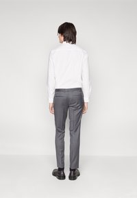 White long-sleeve shirt with button cuffs paired with gray trousers. Slim fit design, smooth fabric, and subtle rear pockets. Black shoes.